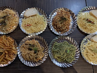 Overhead shot of assorted Italian and Asian pasta dishes on a wooden table.