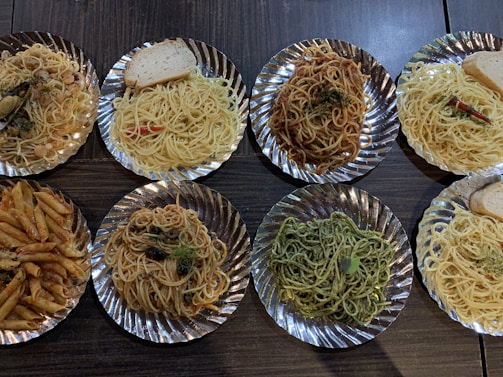 Overhead shot of assorted Italian and Asian pasta dishes on a wooden table.