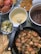 A table spread with assorted dishes including a bowl of cooked crab, a skillet filled with shrimp, chicken, and sliced vegetables, a plate of fried plantains, and bowls of sauces. Lime wedges and tortilla chips are also visible.