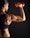 A person with well-defined muscles is lifting a red dumbbell, showcasing strength and fitness against a dark background. The individual's skin is glistening, highlighting their muscular build.