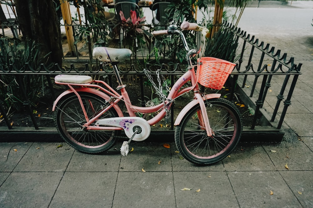 a pink bicycle parked next to a fence