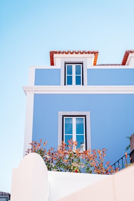 Exterior house wall painted bright blue with white trims on a sunny day