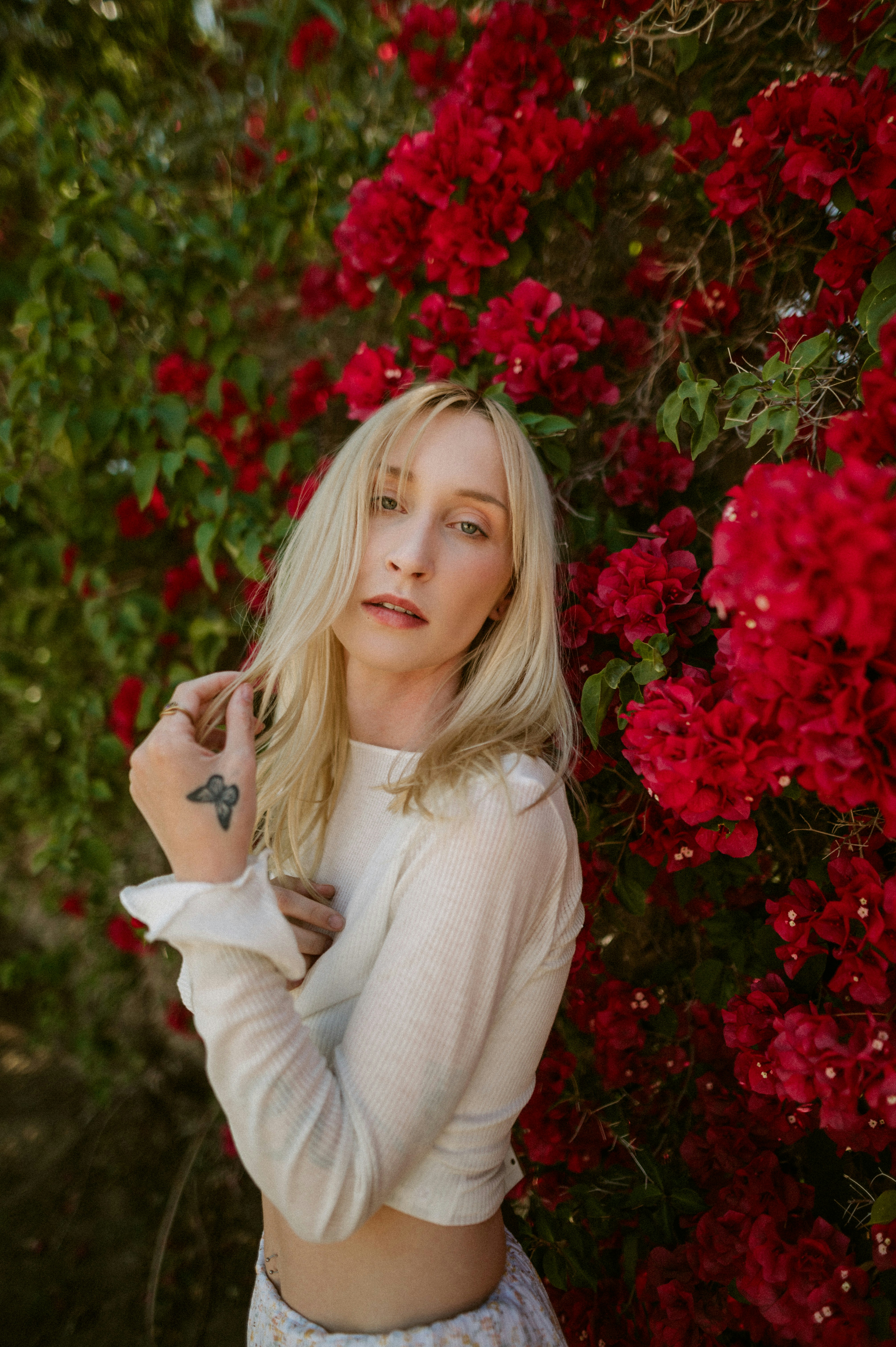 a woman standing in front of a bush of red flowers