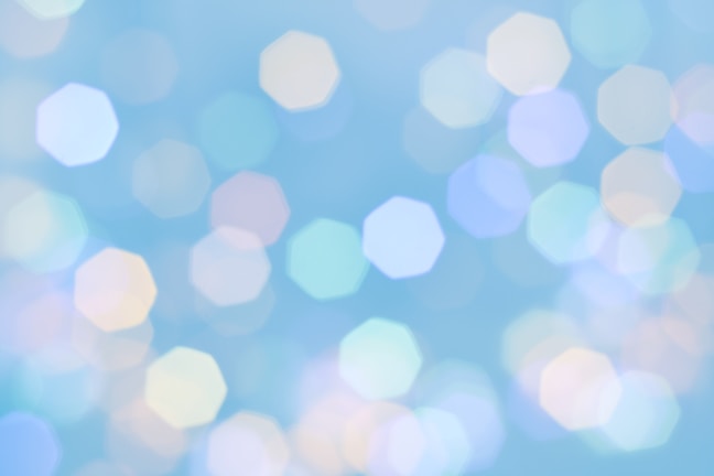 Soft, hexagonal shapes in various pastel colors are scattered across a light blue background, creating a dreamy, blurred effect reminiscent of bokeh photography.