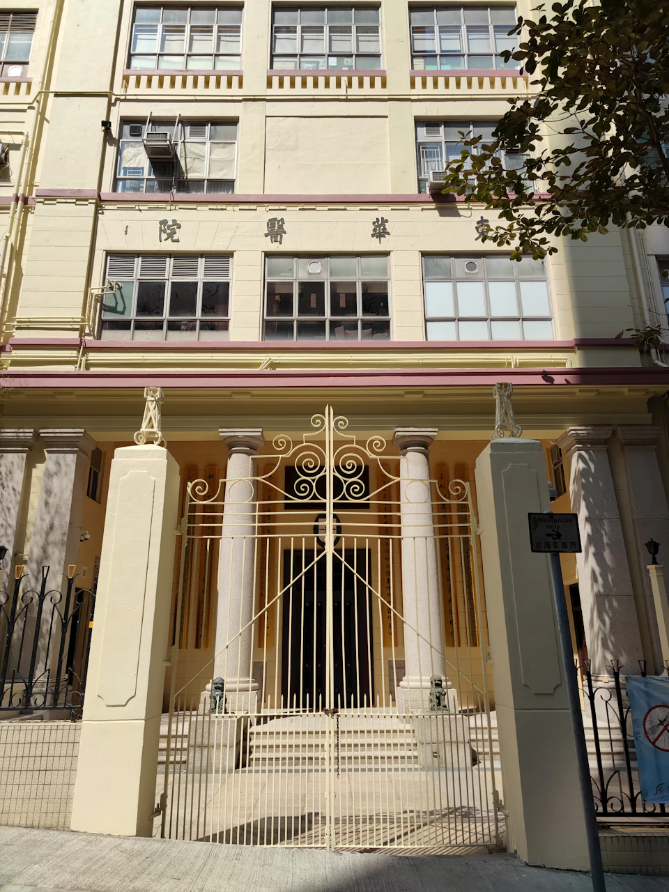 The image shows a large, two-story building with a yellow facade and white trim. The building features numerous windows on each floor, some of which are adorned with ornate ironwork. A black gate stands at the entrance to the building, serving as a boundary between the interior and exterior spaces. In front of the building, there is a staircase leading up to the second floor.