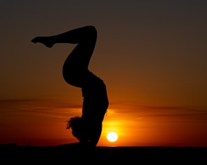 A silhouette of a person practicing yoga against a sunset backdrop.