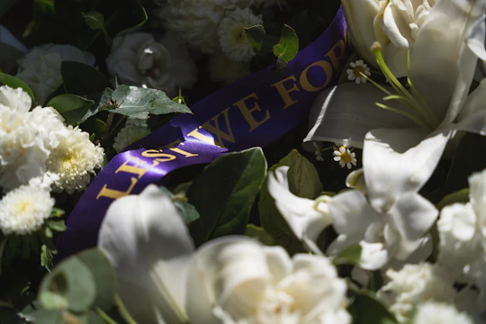 Solemn funeral wreath with white lilies and soft greenery arranged on a clean white backdrop.