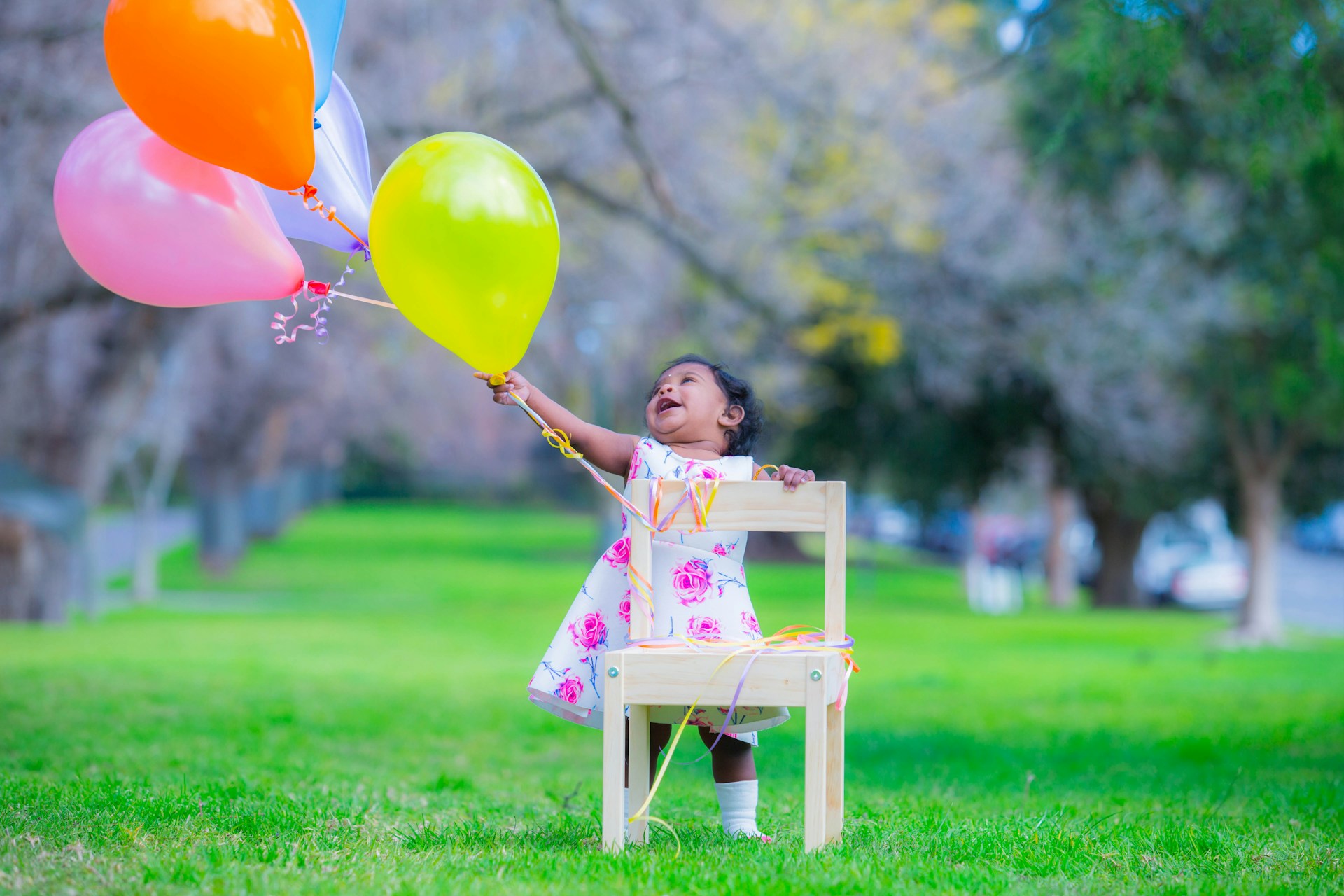 A close-up portrait of a smiling child holding colorful balloons in a sunlit park, capturing pure happiness.