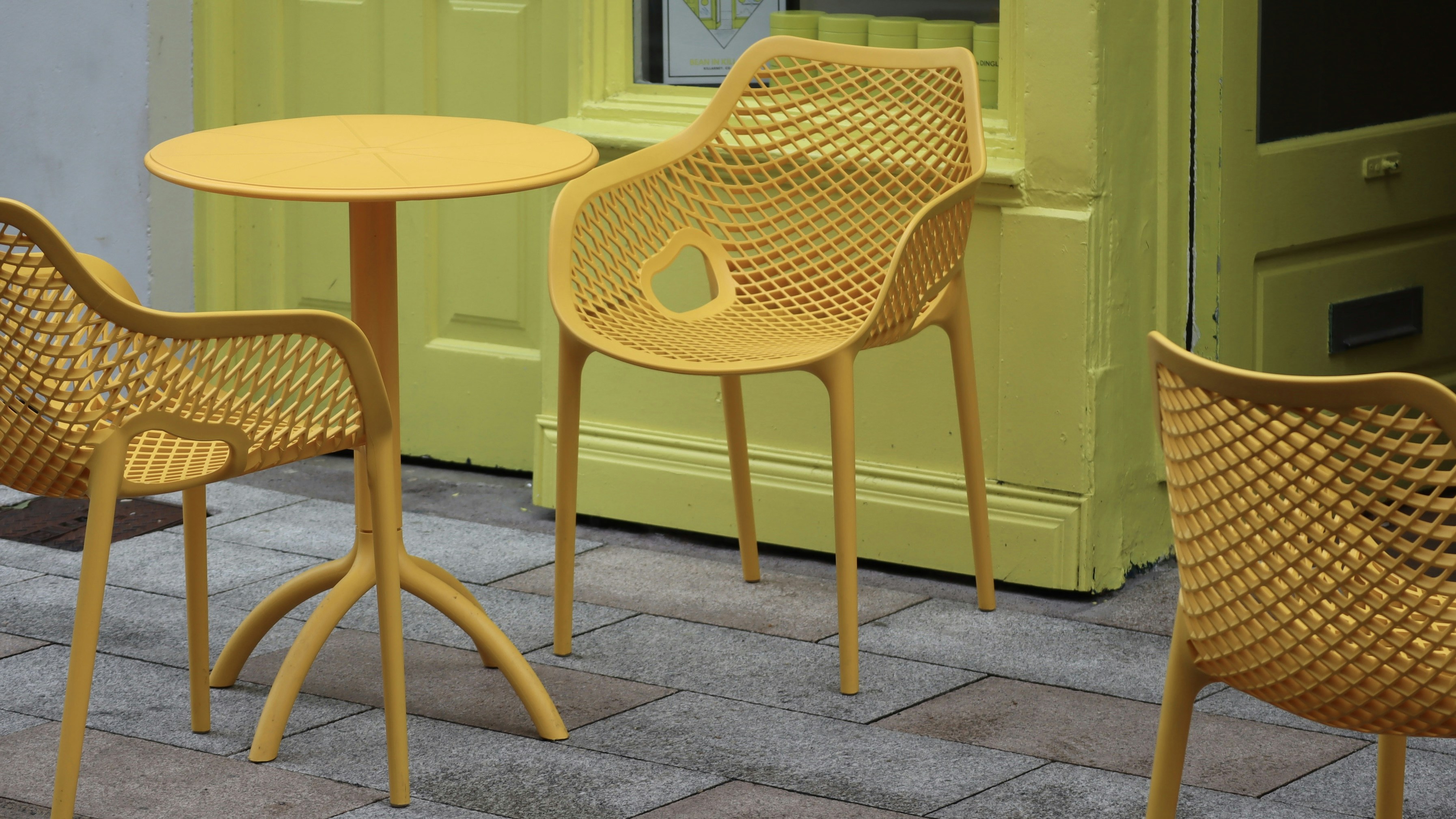 three yellow chairs and a table on a sidewalk