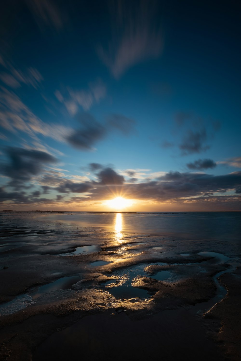 the sun is setting over the water on the beach