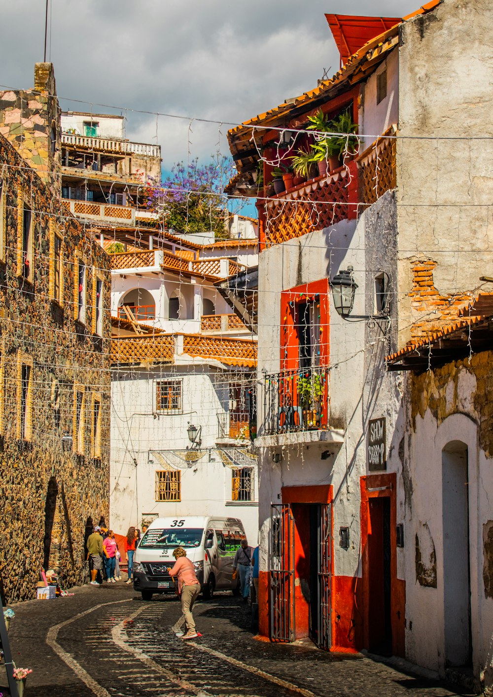 una calle estrecha con gente caminando y coches aparcados a un lado de ella