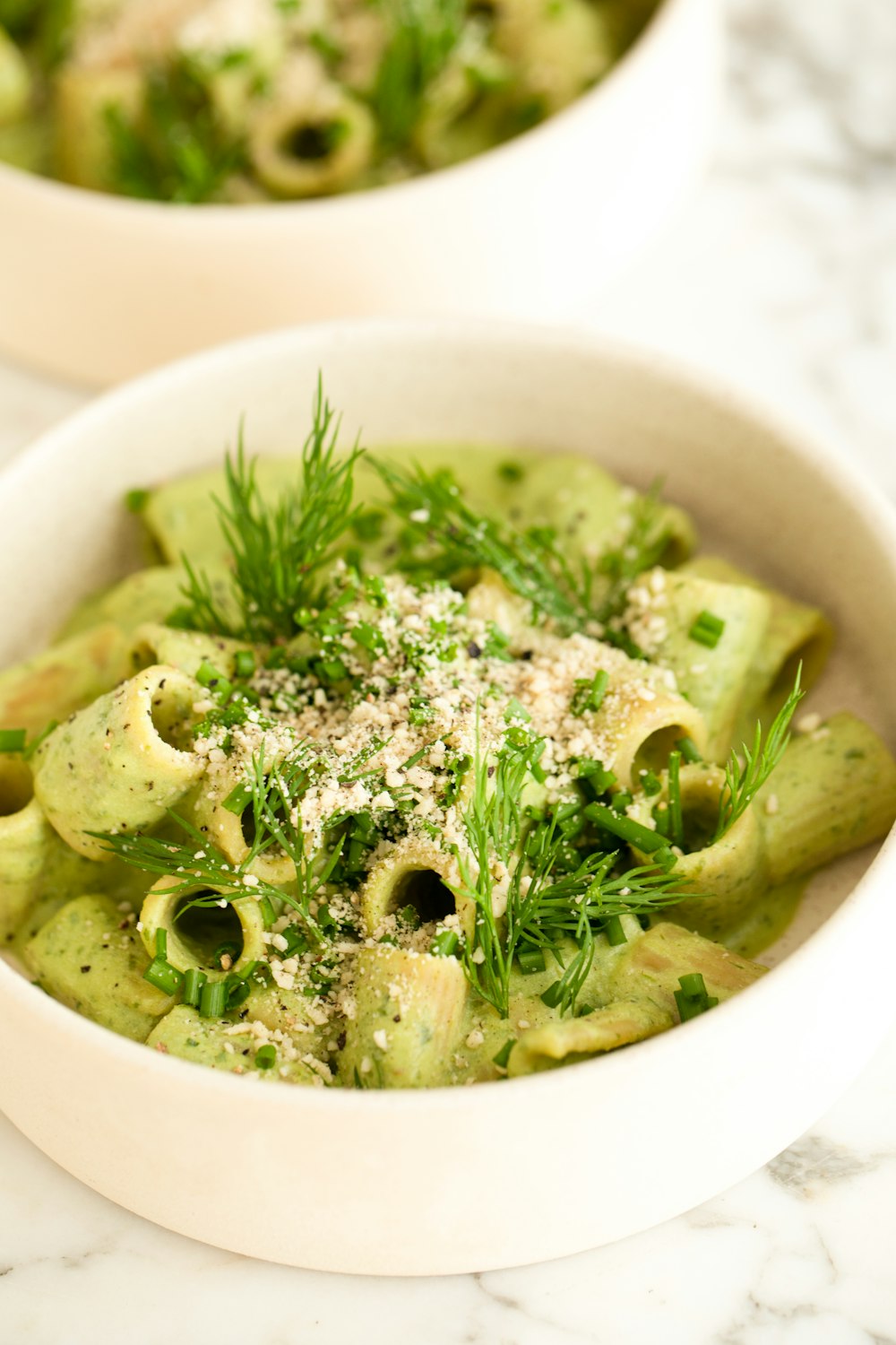 two bowls of pasta with pesto and parsley