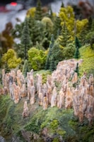 A miniature landscape features detailed rocky formations and lush green trees. Tall, slender rock pillars rise from a grassy terrain, surrounded by various types of dense, fluffy trees resembling a forest. The scene captures a realistic diorama of a natural environment with intricate attention to texture and color.