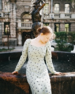 a woman in a dress leaning on a fountain