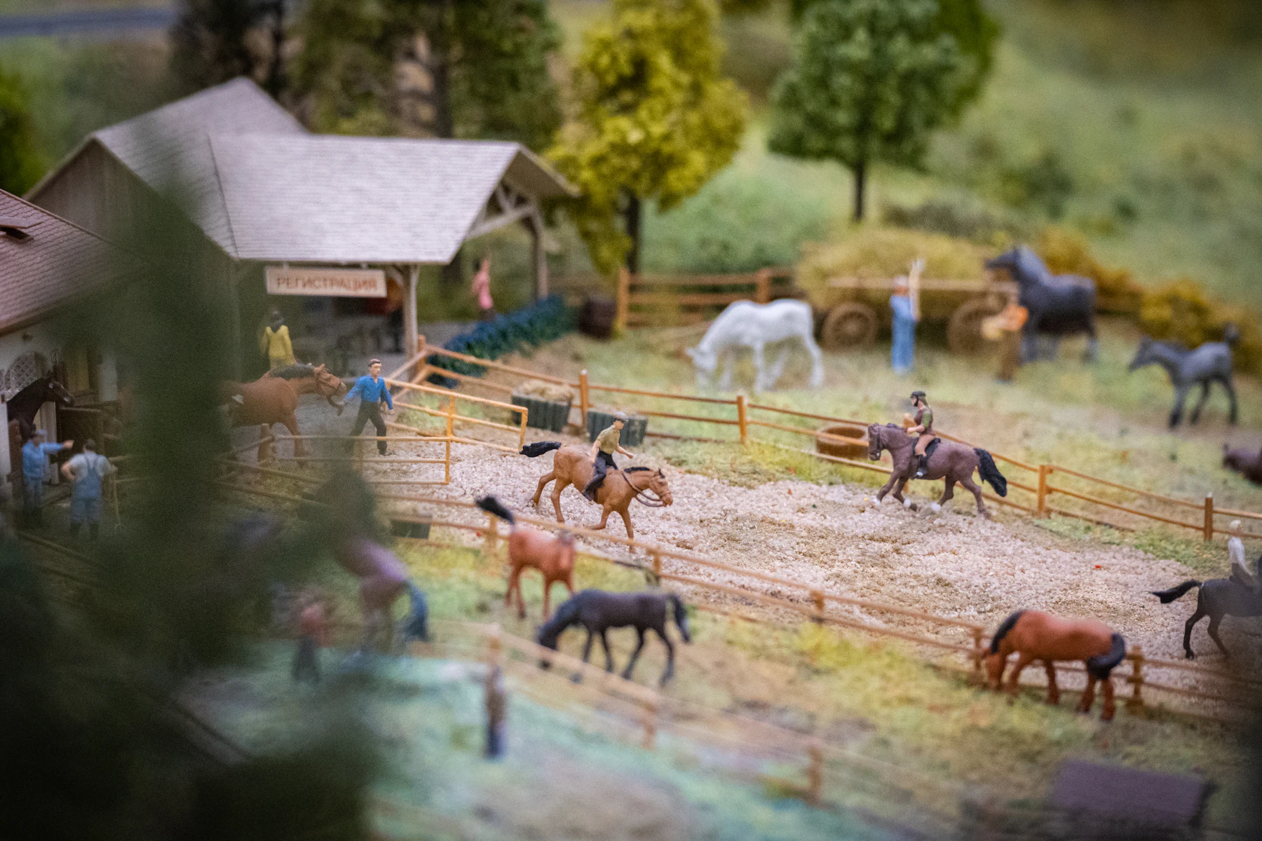 A miniature stable yard with tiny model horses and riders inside wooden fences