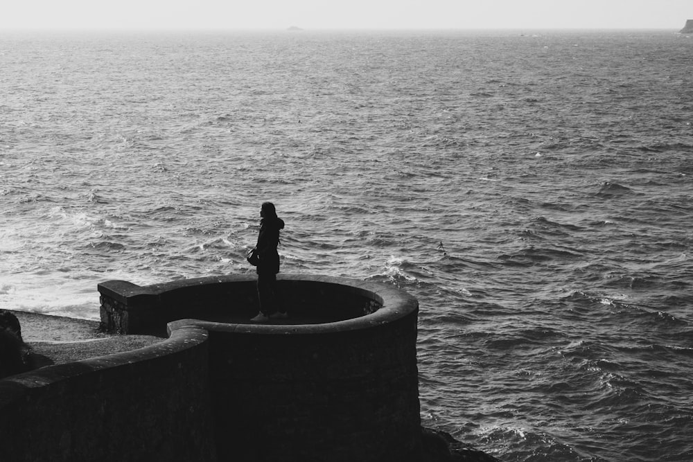 a person standing on the edge of a wall near the ocean