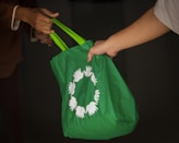 Two people exchanging a green reusable shopping bag with a circular white symbol of birds or hands.