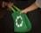 Two people exchanging a green reusable shopping bag with a circular white symbol of birds or hands.