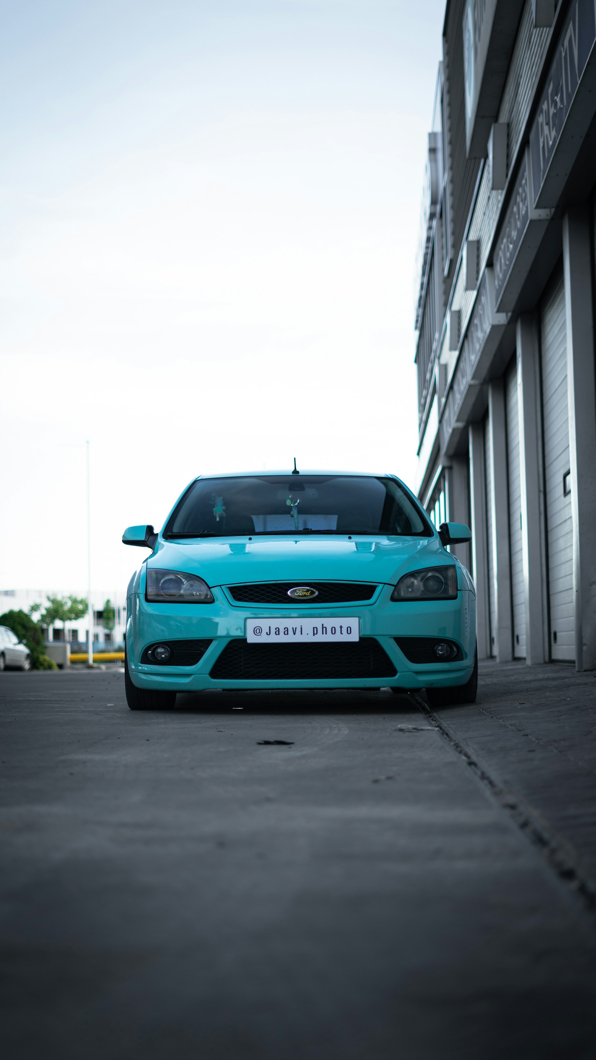 Jaecoo Indonesia vehicle parked in an urban setting with reflections of teal-colored buildings.