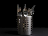 Close-up of argentia silverware clip holding a set of polished forks on a rustic wooden table.