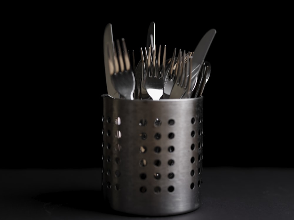 a metal cup filled with forks and spoons