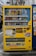 A bright yellow vending machine filled with a variety of beverages including canned sodas, juices, and teas. The machine is placed on an urban sidewalk with signage and colorful labels in Japanese. A notable feature is its cheerful branding with cartoon characters and logos. The immediate background includes elements of a city street, some advertisements, and architectural details.