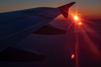 A sleek airplane wing cutting through a glowing sunset sky with warm orange hues.
