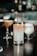 A beautifully arranged collection of cocktails set on a dark wooden table in a sophisticated bar setting. The focus is on a tall glass filled with a light-colored drink, garnished with a slice of dried citrus and a rim coated in chili powder or similar seasoning. Surrounding it are other cocktails in various shapes of glasses, each with a different color and garnish, creating an inviting and upscale atmosphere.