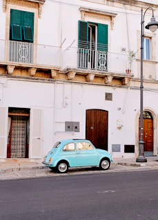 A vintage European classic car parked on a quiet cobblestone street under soft afternoon light.