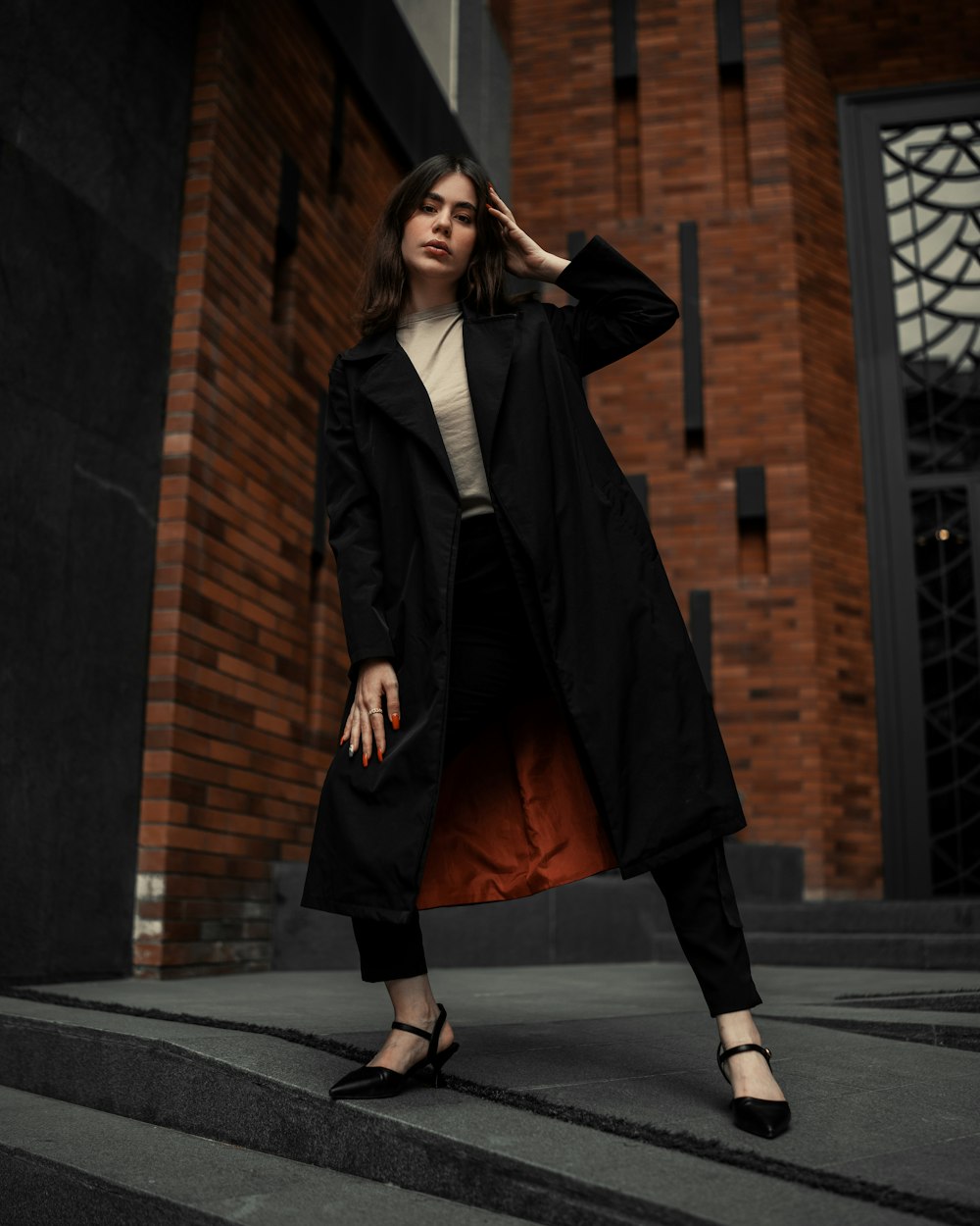 a woman in a black trench coat standing on steps