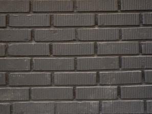 A pattern of horizontally aligned dark grey bricks with a textured surface. Each brick has a uniform size, and the mortar lines create a grid-like structure.