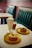 A cozy cafe setting with retro-style teal seating and a tiled wall. On a white table, there are two donuts on yellow plates, one topped with icing and the other with chocolate and sprinkles. There is also a glass of milkshake with whipped cream and a cup of coffee.
