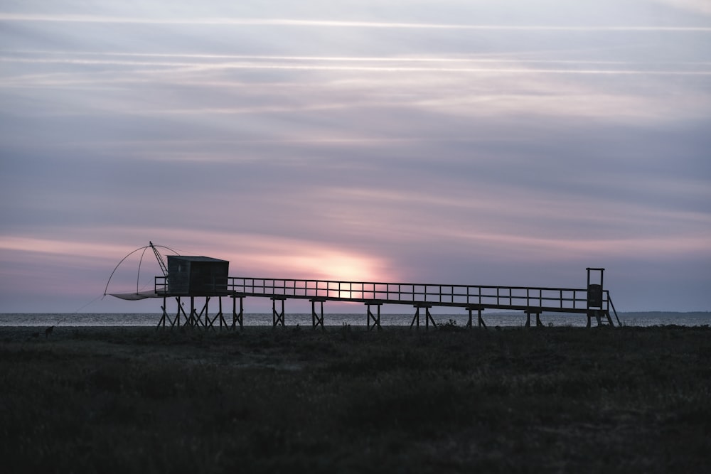 the sun is setting over a pier on the beach