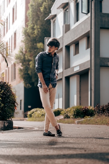 A stylish man wearing a casual shirt and jeans, standing confidently in a sunlit urban street.
