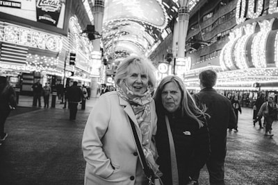 Two friends laughing under neon city lights, caught mid-conversation on a bustling street.