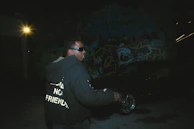 Close-up of a black hoodie with neon green accents and bold graphic prints under urban lighting.