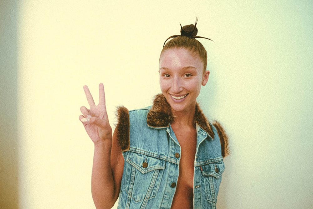 a woman in a jean vest making a peace sign