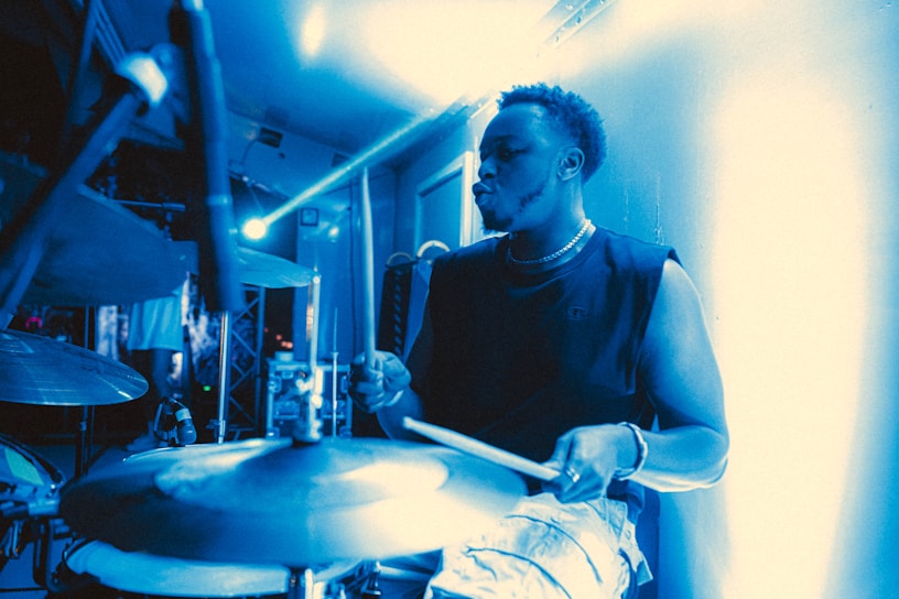 Close-up of Fabs passionately playing drums under blue stage lighting.