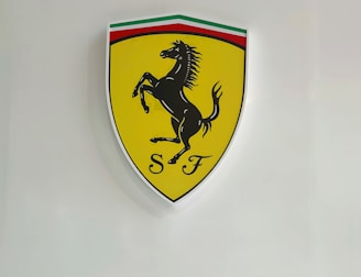 A yellow shield-shaped emblem featuring a black prancing horse with the initials 'S F' below it. The top of the shield has a stripe in green, white, and red, resembling the Italian flag.