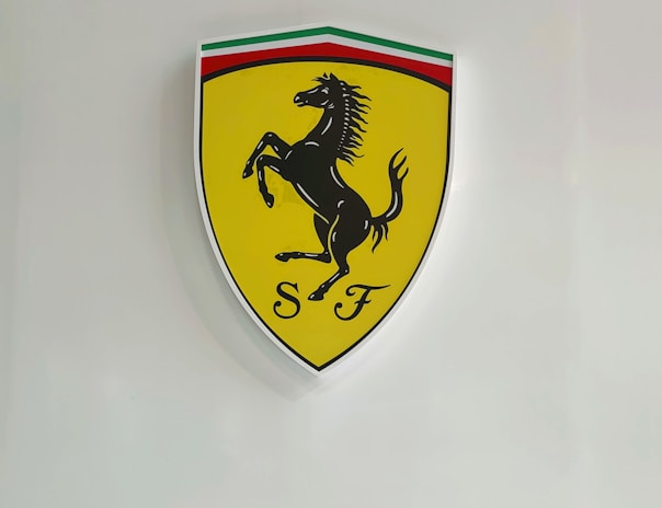 A yellow shield-shaped emblem featuring a black prancing horse with the initials 'S F' below it. The top of the shield has a stripe in green, white, and red, resembling the Italian flag.