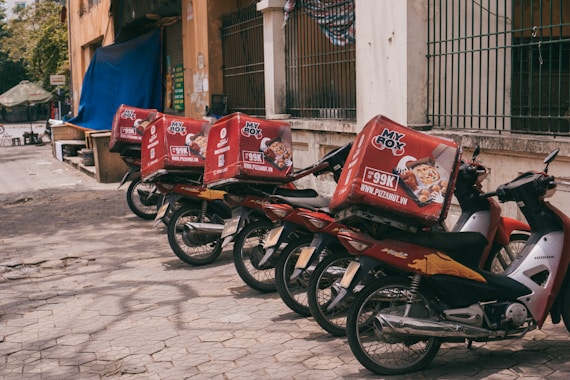 A fleet of motorcycles lined up ready for local deliveries in an urban setting.