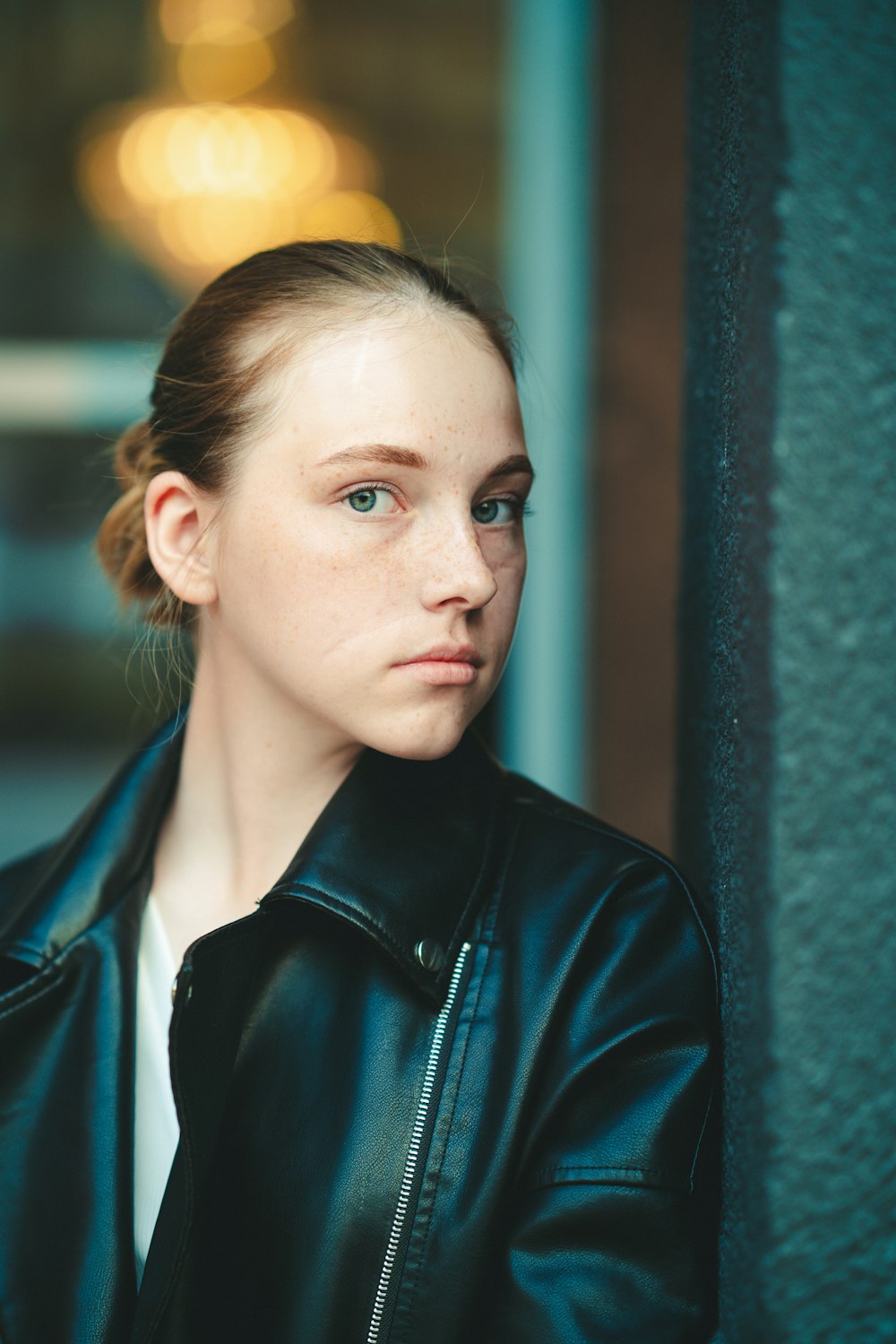 a woman in a black leather jacket leaning against a wall