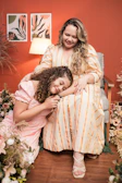 A warm, inviting shot of mother and daughter sharing a laugh over loaded teas in a softly lit pink-themed room.