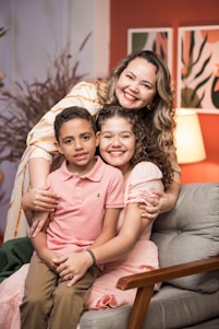 A caring woman with two young children smiling warmly in a bright, clean home setting.