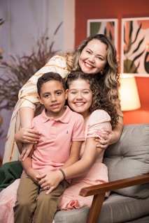 A warm, smiling young Black woman gently playing with two happy children in a cozy living room.