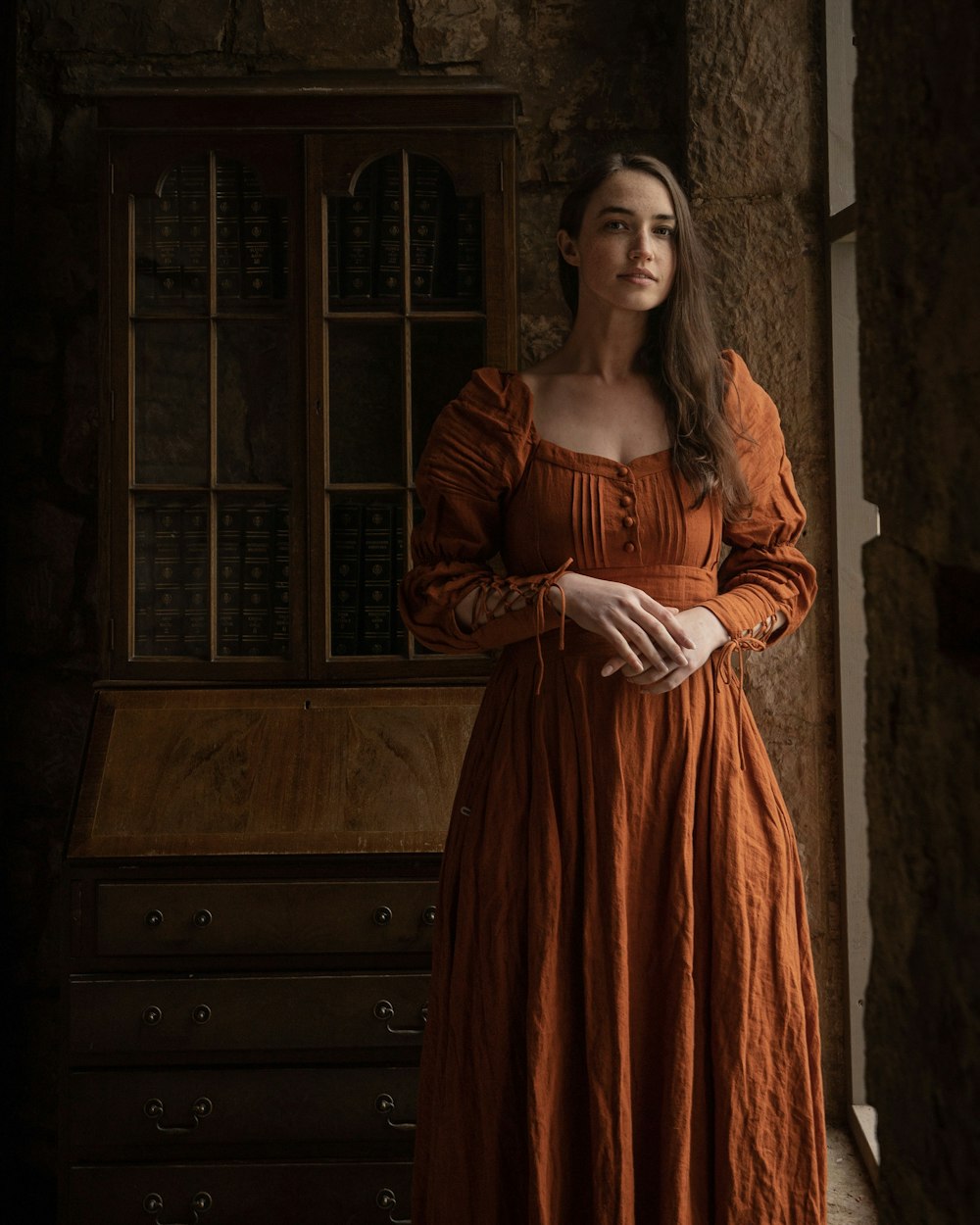a woman in an orange dress standing in front of a dresser