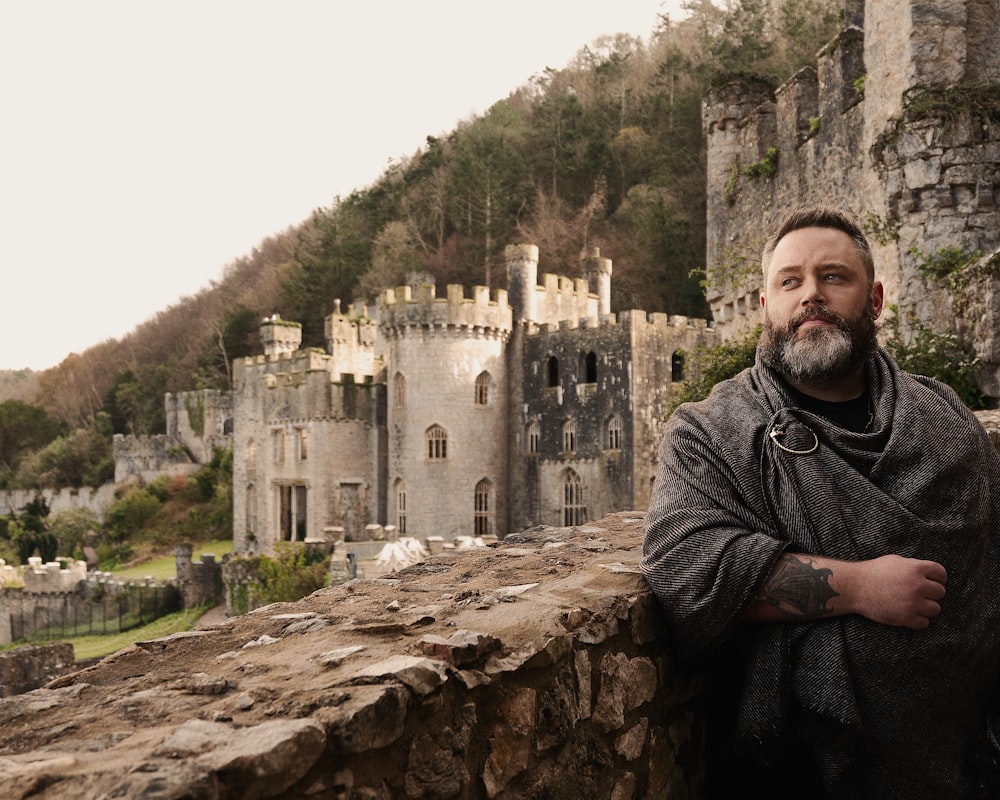 a man standing next to a stone wall near a castle