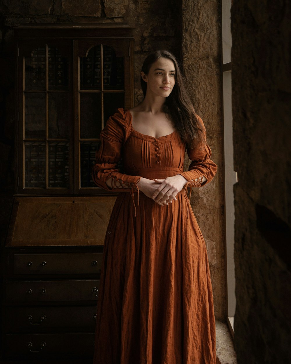 a woman in an orange dress standing by a window