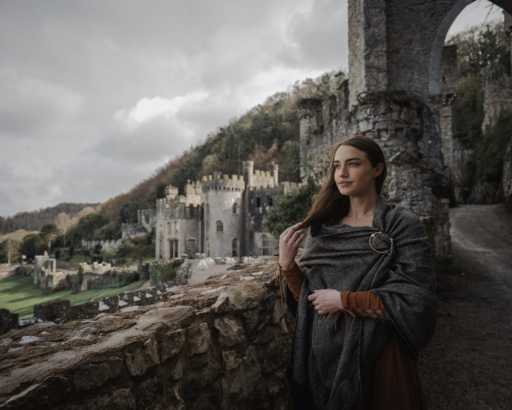 a woman standing on a stone wall next to a castle