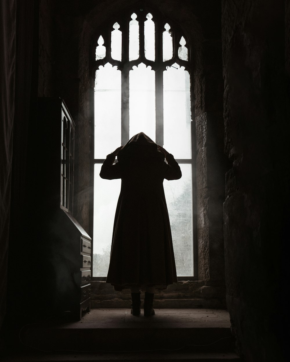 une personne debout devant une fenêtre dans une pièce sombre